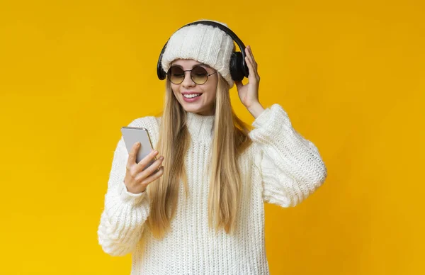 Šťastná dívka ve slunečních brýlích poslouchá hudbu, dívá se na telefon — Stock fotografie