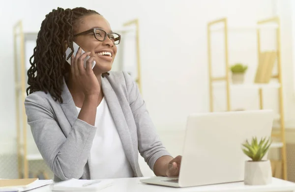Afro ragazza parlando sul telefono seduto al computer portatile in ufficio — Foto Stock