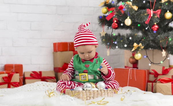 Doce Santa ajudante jogando com decorações de férias sob a árvore de Natal — Fotografia de Stock