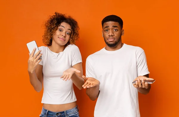 troubles. Puzzled african man and woman with cellphones shrugging