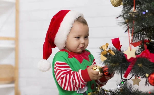 Bebé curioso en traje de elfo mirando las decoraciones de Navidad —  Fotos de Stock