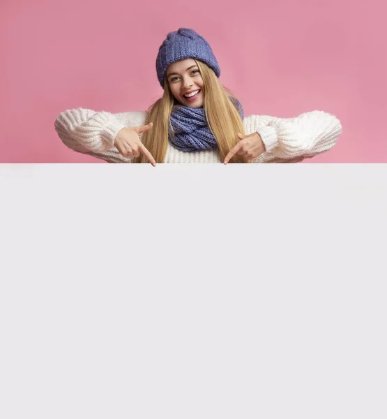 Ξανθιά κοπέλα με το χειμερινό καπέλο που δείχνει λευκό πίνακα — Φωτογραφία Αρχείου