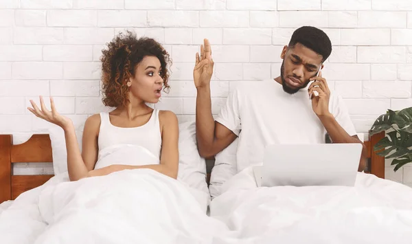 African workaholic husband ingnoring his iiritated wife in bed — Stock Photo, Image