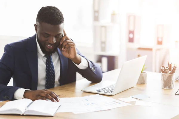 Afro biznesmen sprawdza badania marketingowe, rozmawia przez telefon z asystentem — Zdjęcie stockowe