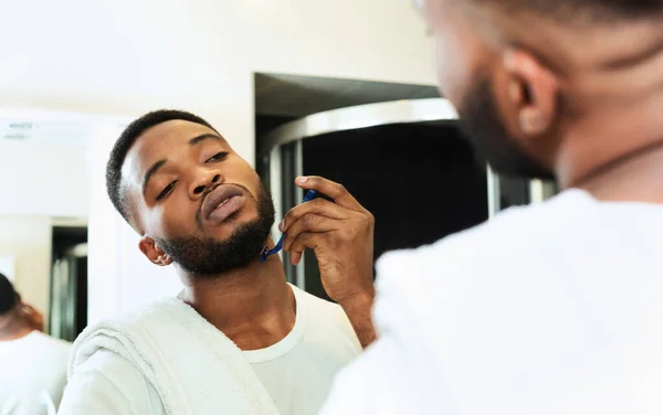 Mladý černošky muž holení vousy, při pohledu na koupelna zrcadlo — Stock fotografie