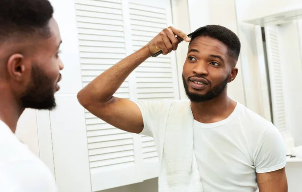 African american guy brushing hair in bathroom