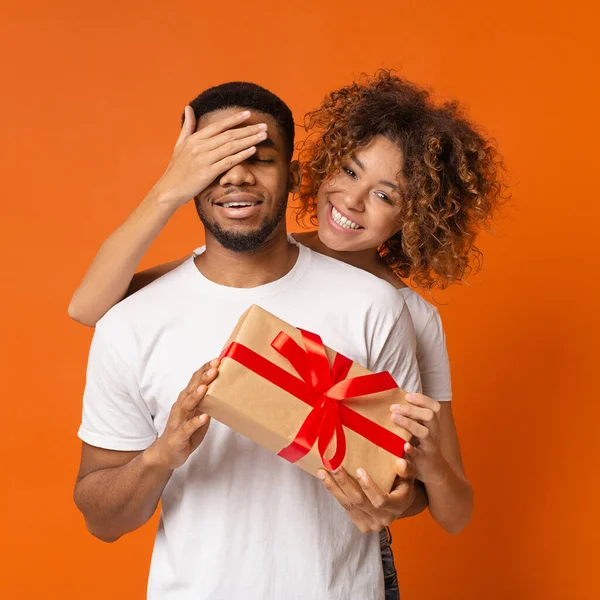 Linda chica africana cubriendo sus ojos de novio y dándole regalo — Foto de Stock