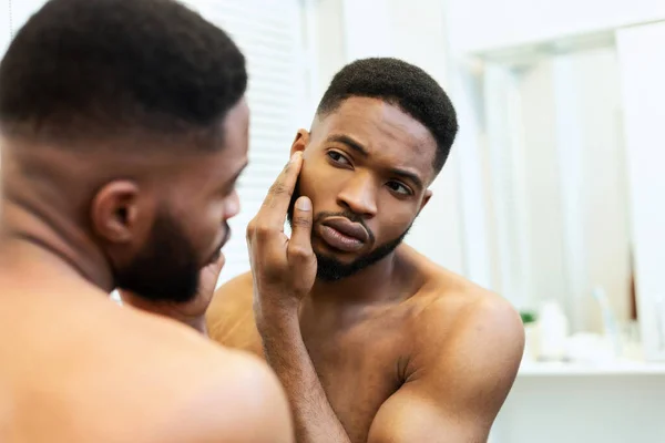 Junger afrikanisch-amerikanischer Kerl überprüft seine Gesichtshaut im Spiegel — Stockfoto