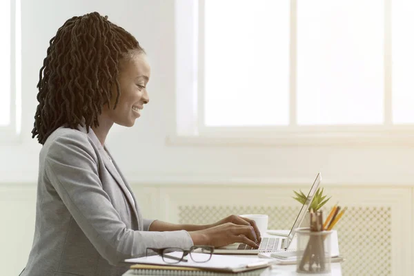 アフリカ系アメリカ人女性がオフィスのノートパソコンで働く、サイドビュー — ストック写真