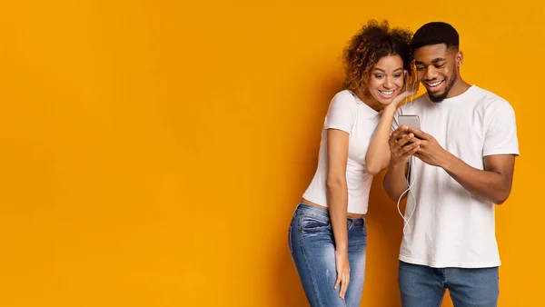 Pareja negra compartiendo auriculares, eligiendo música en la aplicación móvil — Foto de Stock