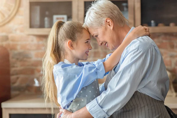 Little granddaughter hugging her happy grandmother in kitchen — Stock Photo, Image