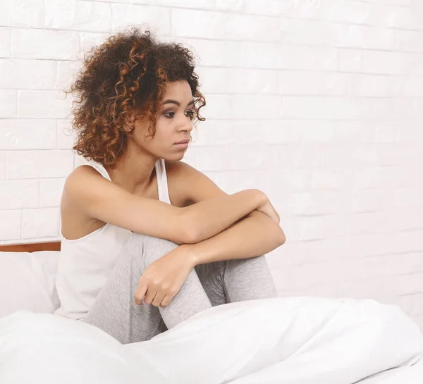 Στεναχωρημένη μαύρη γυναίκα που κάθεται στο κρεβάτι και σκέφτεται τα προβλήματά της — Φωτογραφία Αρχείου