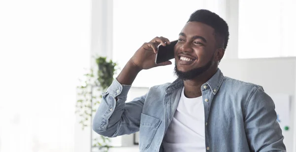 Fröhliche afrikanisch-amerikanische Kerl spricht auf Handy drinnen — Stockfoto