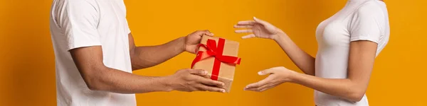 Uomo millenario nero che dà confezione regalo alla donna, panorama — Foto Stock
