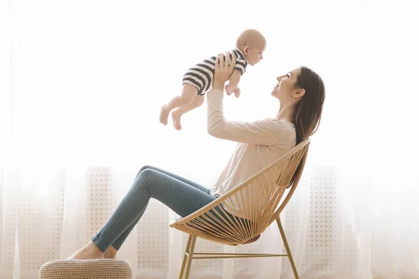 Madre sentada en silla de mimbre y jugando con un niño recién nacido — Foto de Stock