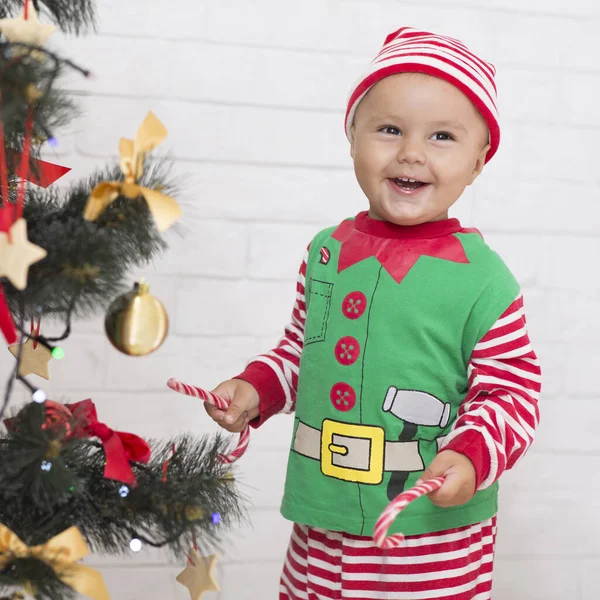 Veselý dětský skřítek hrající si s lízátkem u vánočního stromečku — Stock fotografie