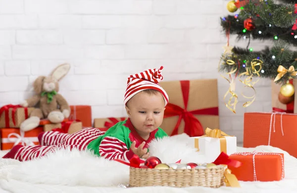 Emotional baby lying under Xmas tree and looking at decorations in amazement Royalty Free Stock Images