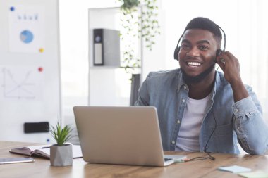 Kulaklıklı gülümseyen bir çalışan ofiste dizüstü bilgisayarda webinar izliyor.