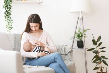 Genç anne bebeğini evdeki kanepede emziriyor.