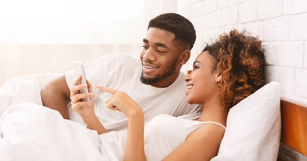 Glücklich liebendes schwarzes Paar vernetzt sich auf Mobiltelefonen im Bett — Stockfoto