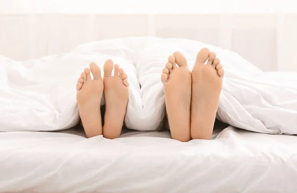 Pies masculinos y femeninos acostados en la cama bajo una manta —  Fotos de Stock