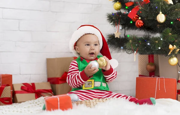 Little baby elf playing with Christmas decorations under Xmas tree — Stock fotografie