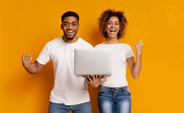 Happy african girl and guy with laptop enjoying good news