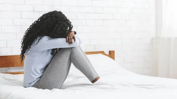 Depressives junges Mädchen sitzt auf dem Bett und umarmt ihre Knie — Stockfoto