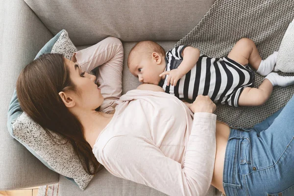 Madre amamantando al bebé recién nacido acostado en el sofá en casa —  Fotos de Stock