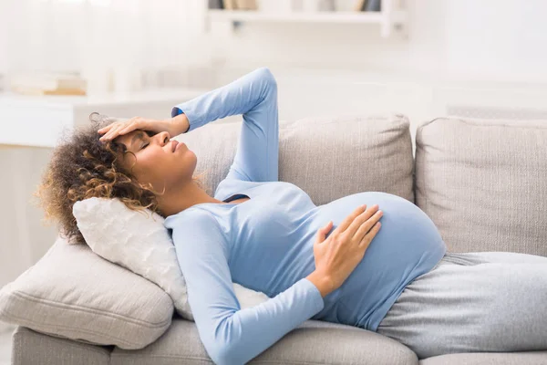 Joven mujer embarazada con dolor de cabeza tumbada en el sofá —  Fotos de Stock