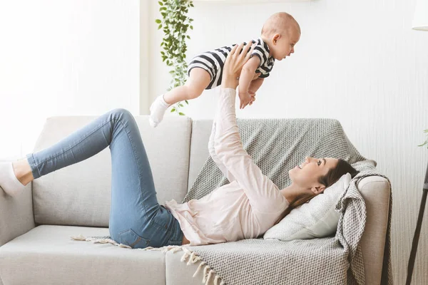 Madre levantando al bebé recién nacido en el aire mientras está acostado en el sofá —  Fotos de Stock
