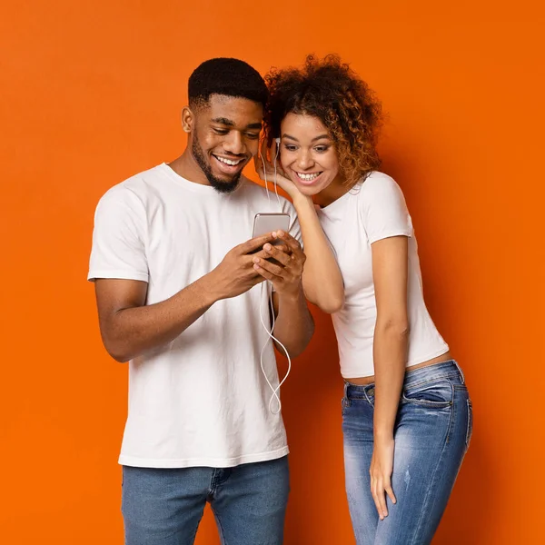 Homme et femme africains joyeux écoutant de la musique sur leur téléphone portable — Photo