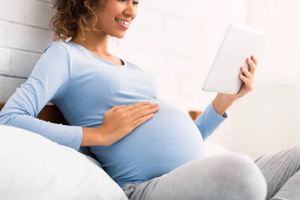 Молода вагітна жінка торкається її живота, використовуючи планшет — стокове фото