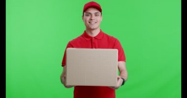 Kırmızı üniformalı arkadaş canlısı kurye kameraya büyük bir paket sunuyor.
