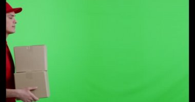 Kırmızı üniformalı neşeli kurye paketlerle yürüyor.