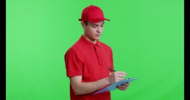 Genç postacı kontrol listesine yazıyor, kameraya gülümsüyor.