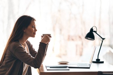 Mutlu gülümseyen kız evde otururken kahve içiyor.