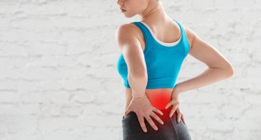 Spor salonunda egzersiz yaptıktan sonra belinde ağrı hisseden genç bir kadın görüntüsü.