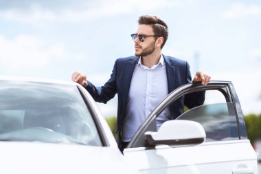 Ciddi bir işletme yöneticisi resmi olarak açık hava arabasının yanında duruyor.