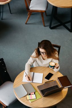 Gözlüklü, dizüstü bilgisayarda çalışan ve notlar alan serbest bir kadın.