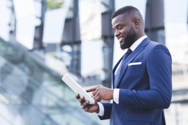 Sayısal Tablet kullanan memnun siyah işadamı açık havada duruyor, anlaşıldı.