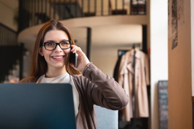 Dizüstü bilgisayarda çalışan ve cep telefonuyla konuşan mutlu kadın serbest yazar.