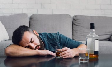 Alkol bağımlılığı. Sarhoş adam uyur masaya yaslanır şişe ve camla
