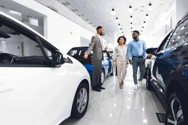 Gerente alegre que mostra o automóvel aos clientes na loja do negócio — Fotografia de Stock