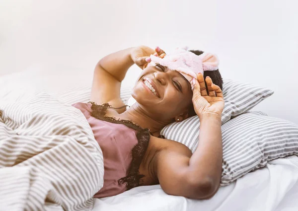 Chica comienza la mañana en la luz del sol, elimina la máscara de dormir en el dormitorio —  Fotos de Stock