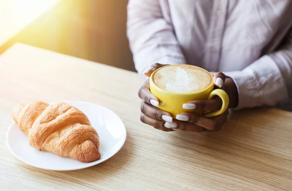 Bonjour paisible. Fille afro-américaine méconnaissable prenant un café avec croissant à table dans un café confortable, gros plan — Photo