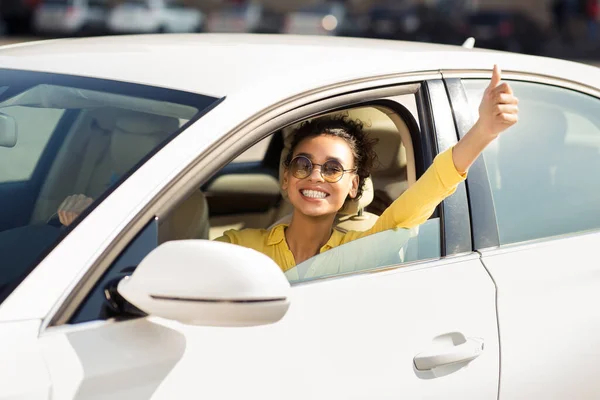 Veselá žena řízení auto gestikulace palce nahoru s jízdou ve městě — Stock fotografie
