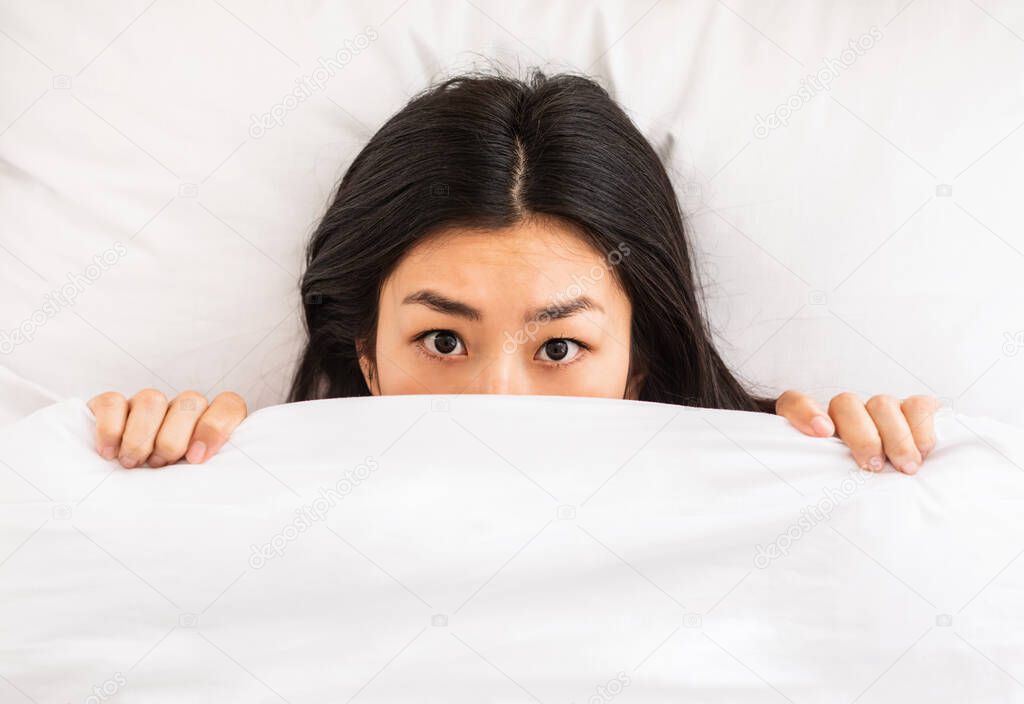 Chinese Girl Peeking Out Of Blanket Lying In Bed, Above-View