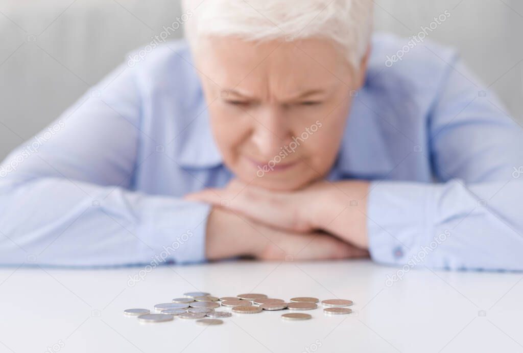 Elderly Poverty. Depressed senior woman looking at last coins lying at table