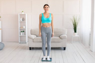 Sıska kadın evde tartıya çıkıp kendini tartıyor.